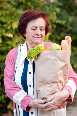 Older woman holding grocery bag standing outdoor