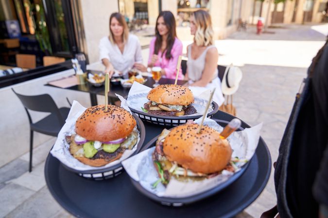 Crop waiter serving burgers for female clients on street