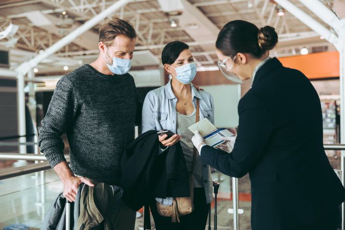 Man and woman with airlines staff at boarding gate of airport during pandemic