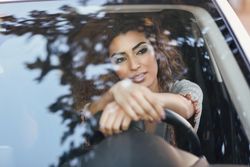 Smiling woman with curly hair sitting in car with hands on steering wheel