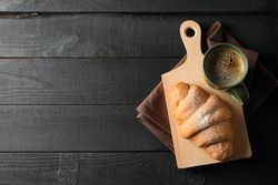 Board with croissant and mug of coffee on dark wooden background, copy space