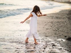 Adorable girl walking and playing on seaside at sunset