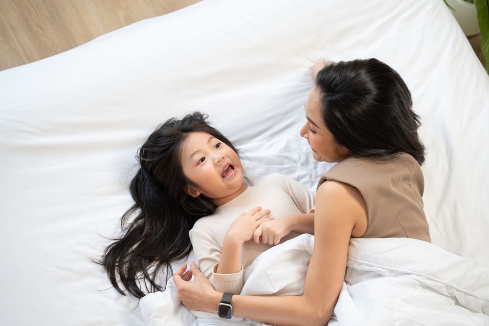 Top view of Asian mother and daughter cuddle and talking on bed.
