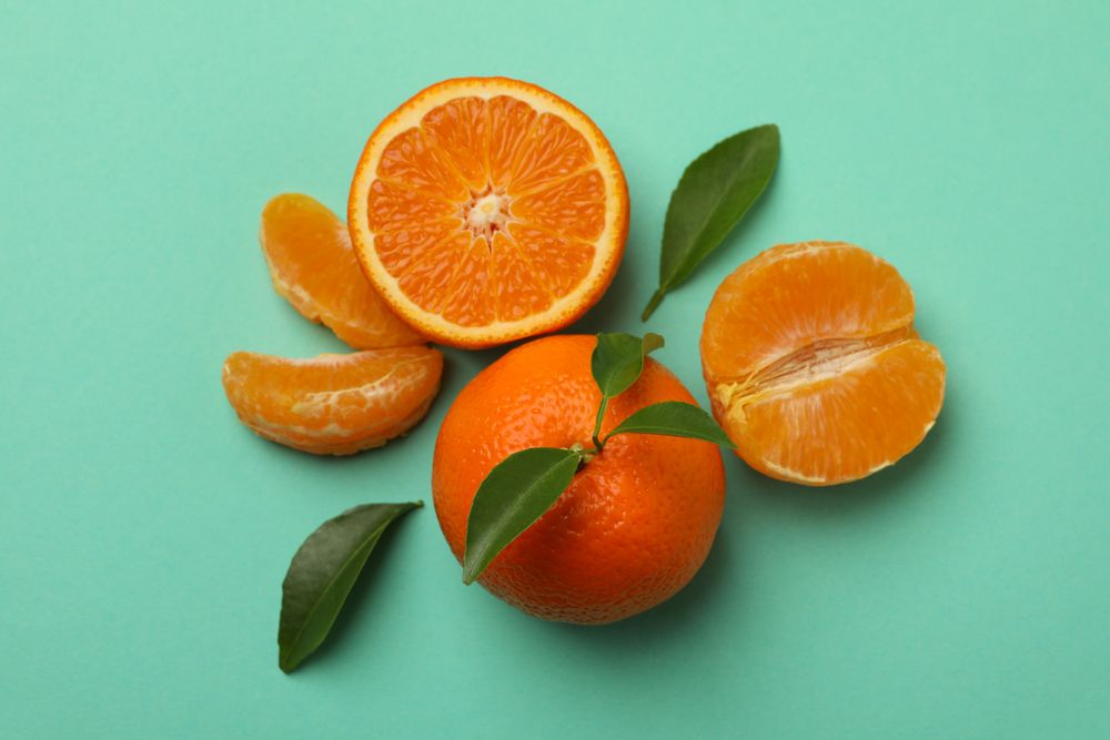 Ripe mandarins with leaves on mint background, top view
