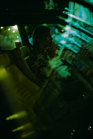 Side view of young man sitting in an old car at night