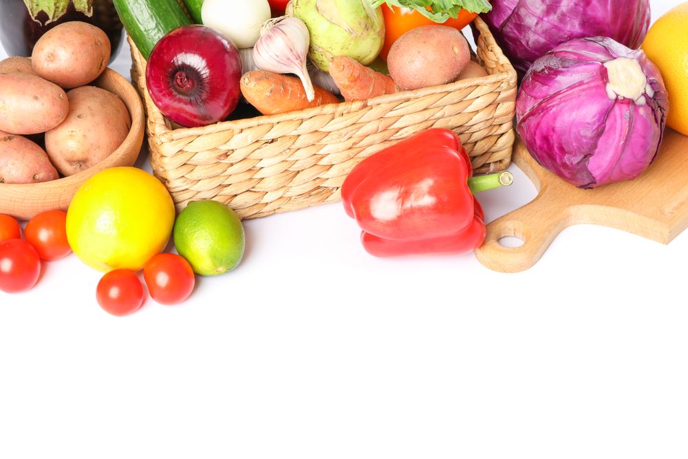 Wicker basket, wood board and vegetables isolated on blank background