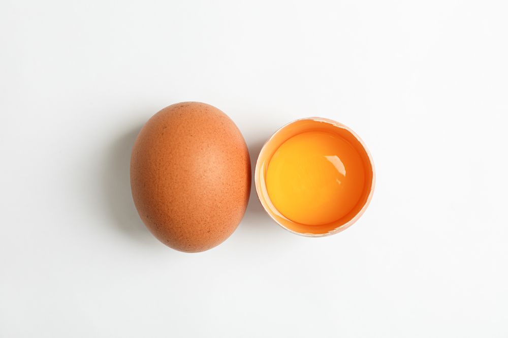 Whole egg and half egg with yolk on blank background, space for text and top view