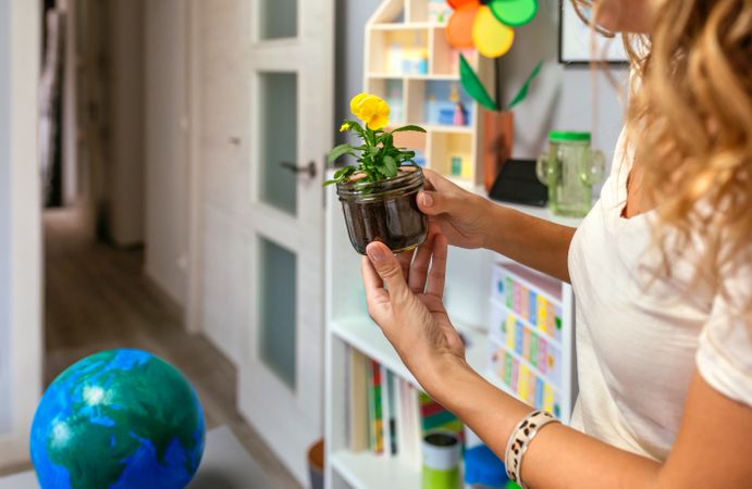 Woman holding a pansy plant inside of glass pot in ecology classroom