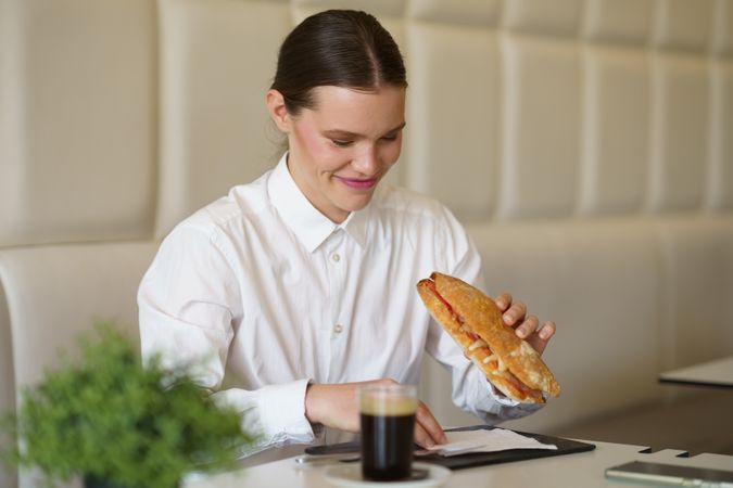 Businesswoman eating a sandwich and drinking coffee in a cafeteria