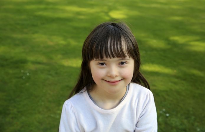 Beautiful little girl sitting at the park with grass behind