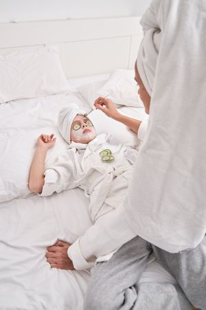 Mother applying facial mask on child during spa session