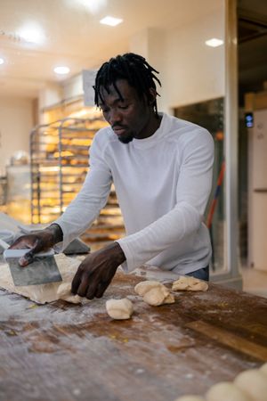 Black baker cutting dough with scapula