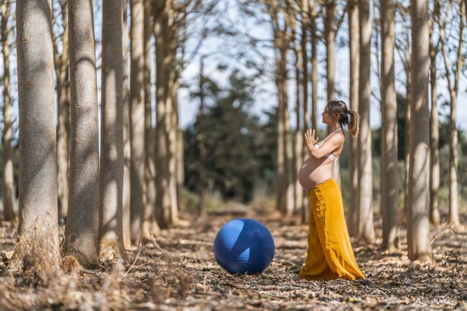 Adult pregnant woman training with pilates ball in park during sunny day