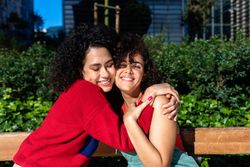 Female couple smiling while in love hugging in city park