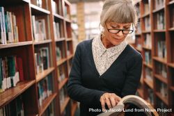 Mature woman going through a reference book in a university library bGxLY0