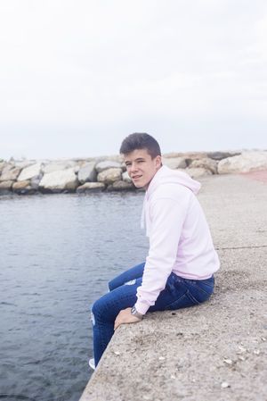 Young teenager male sitting on breakwaters while looking at camera