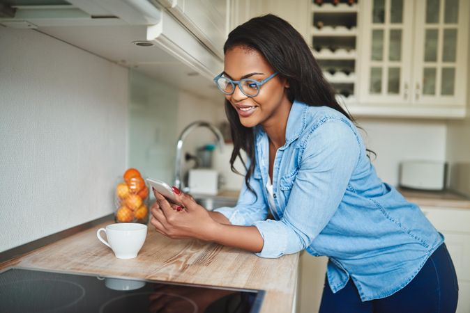 Woman smiling at phone with a cup of tea in her kitchen