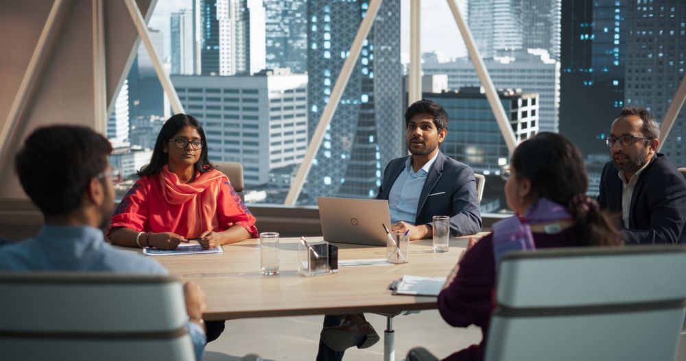South Asian Colleagues Sitting Behind a Conference Table in a Meeting Room in a Modern Office Building