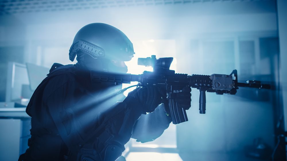 Close Up Portrait of Masked Squad Member of Armed SWAT Police Officers Who Storm a Dark Seized Office Building with Desks and Computers