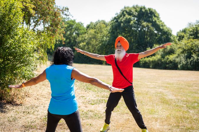 Mature Sikh couple doing jumping jacks in park