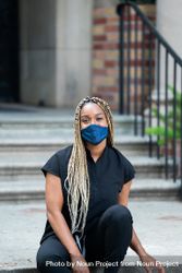 Portrait of healthcare worker sitting outside wearing scrubs and mask looking at camera 4NEDg5