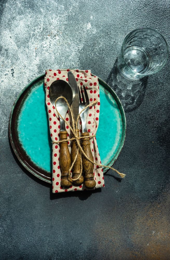 Teal table setting with silverware wrapped in red dotted napkin