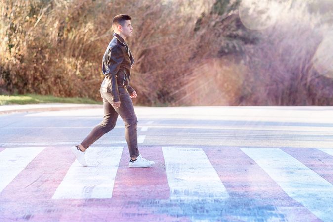 Teenage male wearing a leather jacket walking on crosswalk