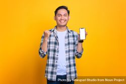 Happy Asian male receiving good news from blank screen of smart phone in studio shoot 4ZZL34