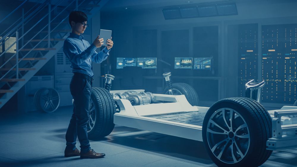 Automobile Engineer Working on Electric Car Chassis Platform, Using Tablet Computer Augmented Reality with 3D CAD Software Modelling.