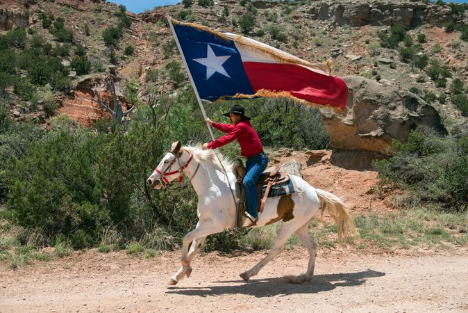 Man with Texas flag aboard white stallion, performing at the Pioneer Amphitheater, Amarillo, Texas