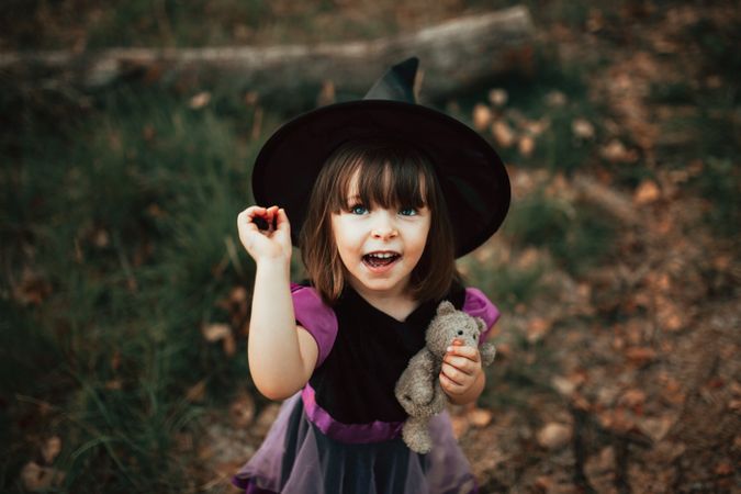 Girl in witch costume looking up with her teddy bear