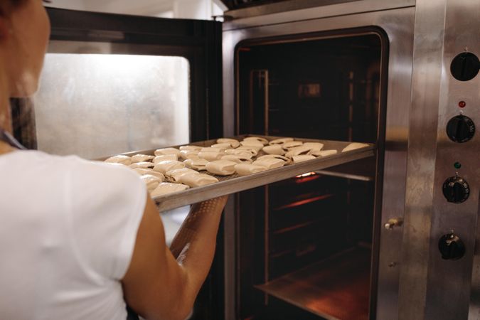 Female baker putting a baking tray full of rolls in oven