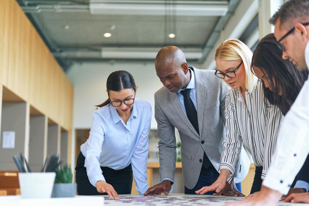 Group of people huddled over a puzzle in an open bright office