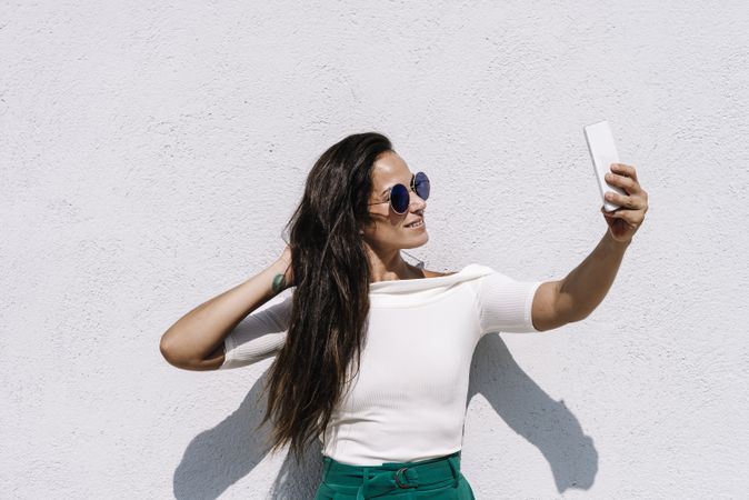 young female in trendy outfit posing for selfie while standing on bright background