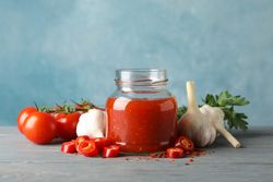 Jar with red chilli and tomato sauce, and spices on wooden table