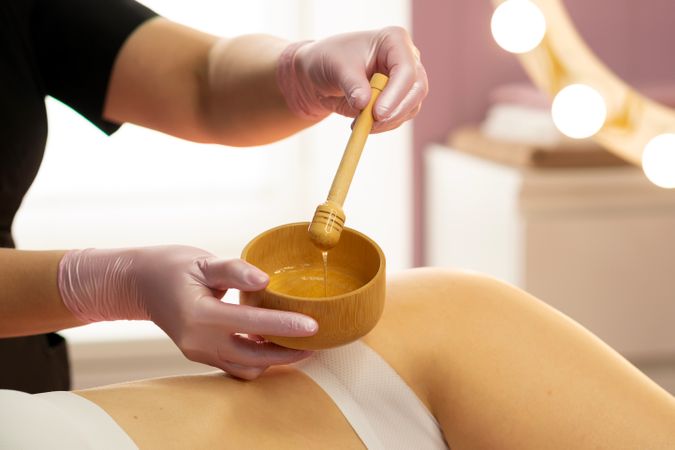 Beautician applying warm honey treatment during spa body therapy.