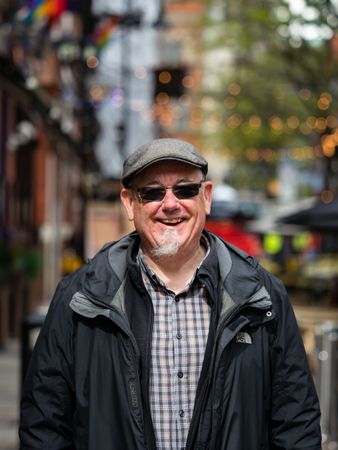 Happy man standing outside in sunglasses and hat, vertical