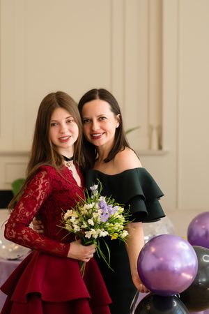 Teen girl holding bouquet flowers standing with woman.