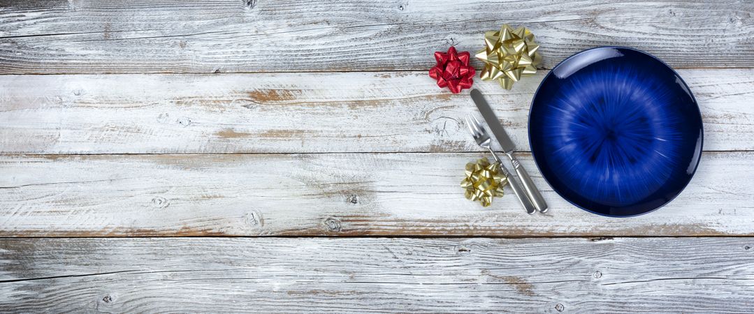 Basic table setting of an empty main dark blue dish with cutlery on wood plus holiday decorations