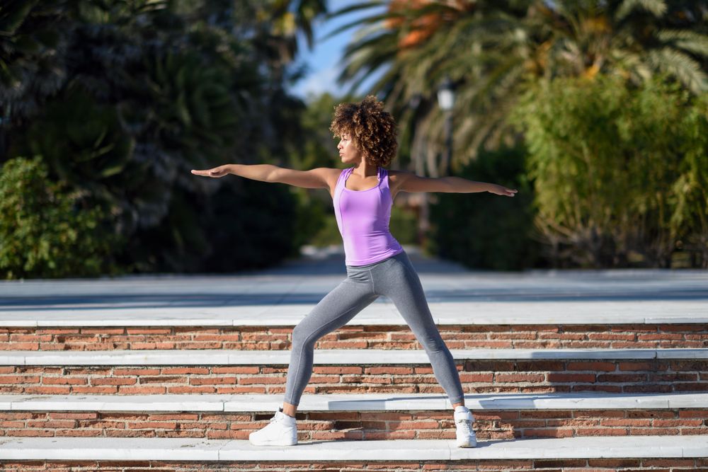 Black woman with afro hairstyle doing yoga on promenade