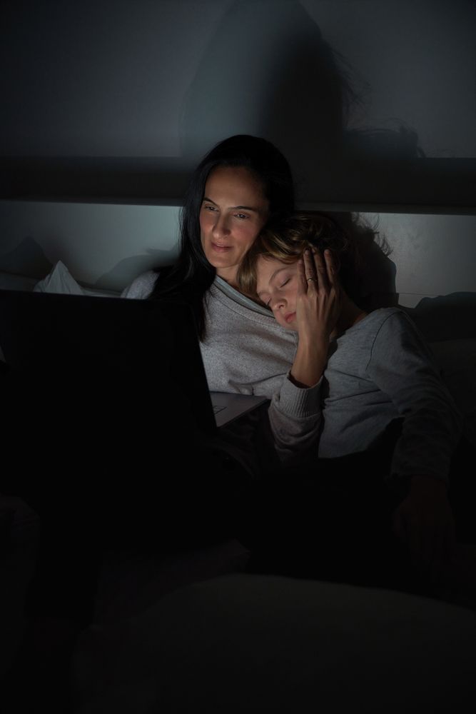 Mother helping sleepy son to do homework in darkness