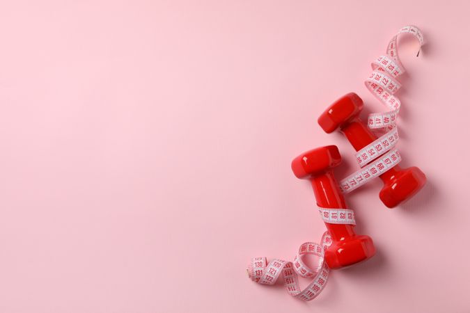 Dumbbells and measuring tape on pink background, space for text