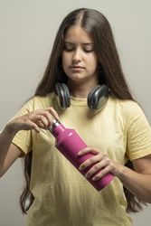 Teenage girl holding pink water bottle with headphones around neck in natural beauty portrait