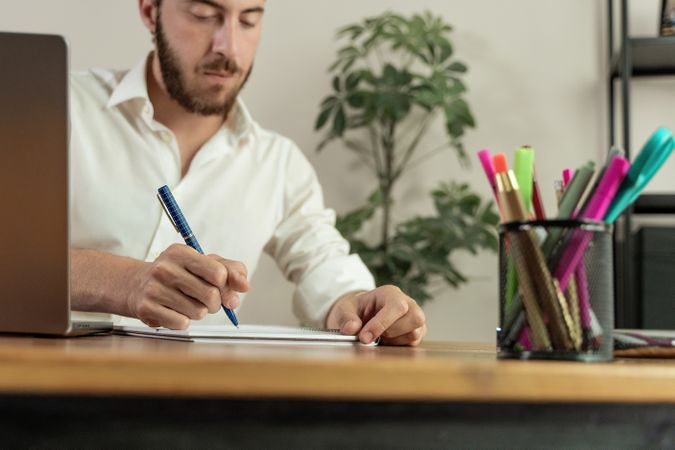 Close up of a man writing in a notebook at his desk.