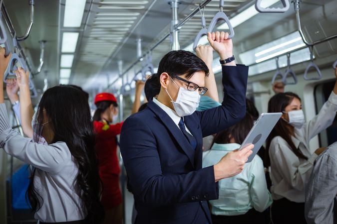 Businessman standing reading digital tablet in busy metro car