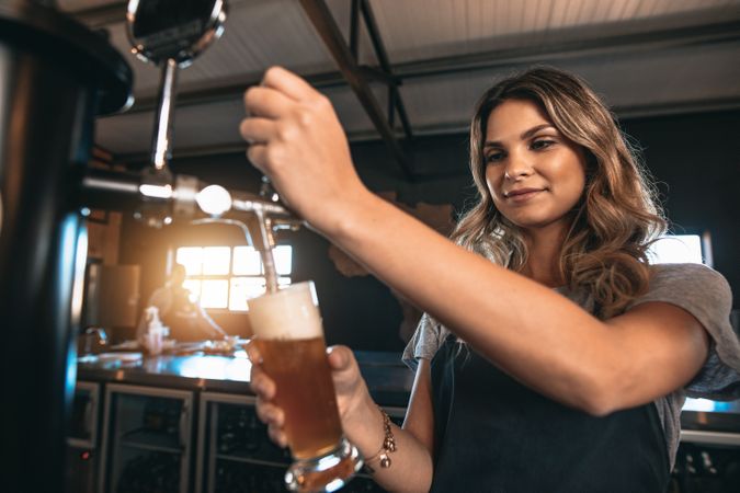 Young woman dispensing beer in bar from metal spigots