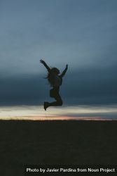Silhouette of a woman jumping in a field with her arms up and knees bent bGR7a4