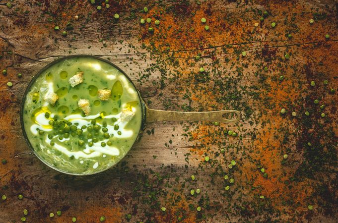 Green vegetable cream soup with crackers and peas in a pan