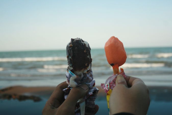 An ice cream cone in each hand looking out to the beach