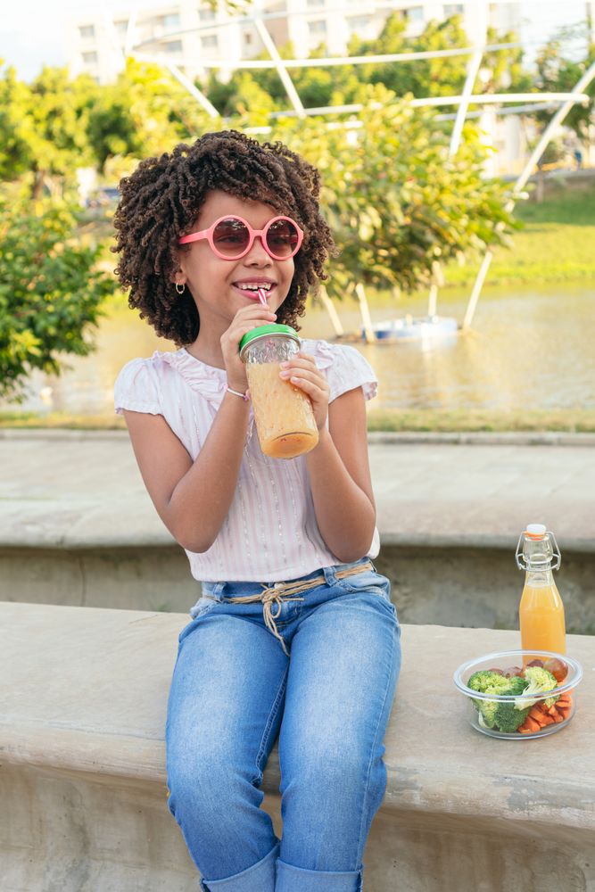Girl with afro hair drinking milkshake in the park. Healthy eating